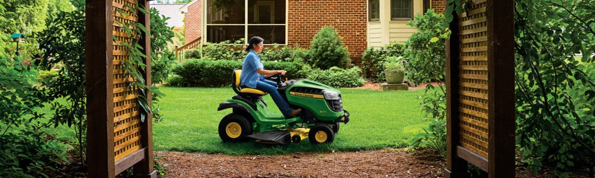 A woman on a John Deere lS240 Select Series mowing a lawn in a vibrant garden.