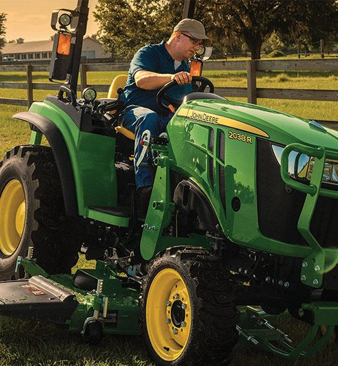 Man riding a John Deere mower on a farm at dusk.